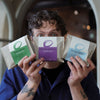 Person holding three packages of Alberto Calderon coffee in front of their face with a blurred background